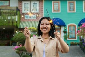 portrait of beautiful happy young asian woman holding sparklers fireworks to celebrate new year eve with garden party standing in outdoor vintage house yard photo