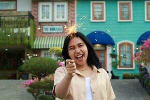 portrait of beautiful happy young asian woman holding sparklers fireworks to celebrate new year eve with garden party standing in outdoor vintage house yard photo