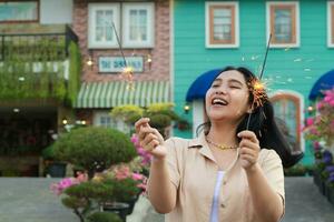 portrait of beautiful happy young asian woman holding sparklers fireworks to celebrate new year eve with garden party standing in outdoor vintage house yard photo