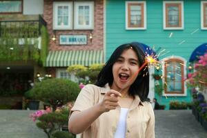 portrait of beautiful happy young asian woman holding sparklers fireworks to celebrate new year eve with garden party standing in outdoor vintage house yard photo