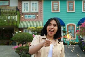 portrait of beautiful happy young asian woman holding sparklers fireworks to celebrate new year eve with garden party standing in outdoor vintage house yard photo