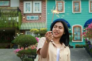 portrait of beautiful happy young asian woman holding sparklers fireworks to celebrate new year eve with garden party standing in outdoor vintage house yard photo