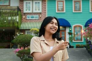 portrait of beautiful happy young asian woman holding sparklers fireworks to celebrate new year eve with garden party standing in outdoor vintage house yard photo