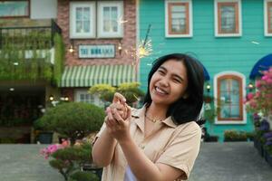 new year eve celebration concept. attractive asian young woman holding sparkler with laughing happy in outdoor garden of vintage house yard photo