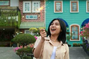 portrait of beautiful happy young asian woman holding sparklers fireworks to celebrate new year eve with garden party standing in outdoor vintage house yard photo