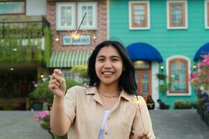 cheerful young asian woman holding sparkler to celebrate new year eve with garden party standing over colorful vintage house yard photo