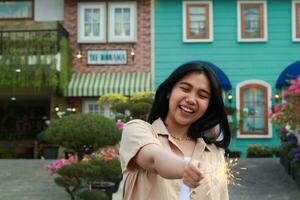 new year eve celebration concept. attractive asian young woman holding sparkler with laughing happy in outdoor garden of vintage house yard photo