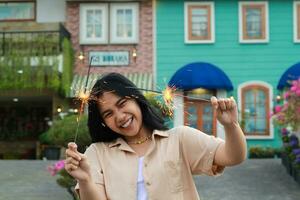cheerful young asian woman holding sparkler to celebrate new year eve with garden party standing over colorful vintage house yard photo