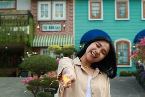 new year eve celebration concept. attractive asian young woman holding sparkler with laughing happy in outdoor garden of vintage house yard photo