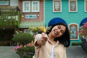 happy young asian woman holding sparkler enjoy new year eve celebration in outdoor garden of colorful vintage house in evening photo