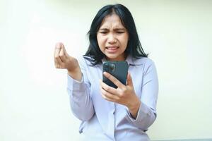 decepcionado bonito asiático joven negocios mujer utilizando mano teléfono con levantamiento mano vestir formal traje, aislado en blanco foto