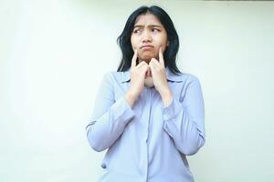 sad worried asian young woman looking away with thoughtful expression and thouching her cheek with forefinger isolated over white background photo