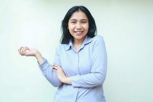 smiling beautiful asian young business woman presenting gesture showing to empty space with open palm and look at camera with crossed arm isolated over white background photo