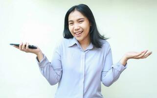 happy asian young business woman holding mobile phone and spreads palm sideways considering product offering, smiling to camera satisfied expression, wear formal shirt, isolated on white background photo
