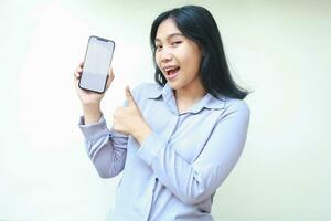 pretty smiling asian young business woman holding mobile phone with empty screen giving thumbs up, approval and good sign gesture, show app and product wear formal shirt isolated on white background photo