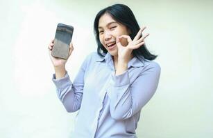 excited asian young business woman holding cell phone with empty screen with ok sign gesture, showing imaginary product, smiling female look camera wearing formal shirt isolated in white background photo