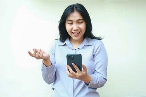 excited young asian business woman using smartphone to video call online meeting wearing formal shirt with raising open palm, explaining gesture, standing over isolated white background photo