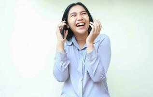 portrait of ecstatic asian young business woman laughing speaking on mobile phone, successful female raising arm look away rejoicing, wear formal office shirt standing over isolated white background photo