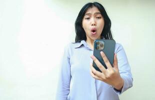 shocked asian young business woman stunned with wow expression looking to mobile phone hold on hands wearing formal shirt standing over isolated white background photo