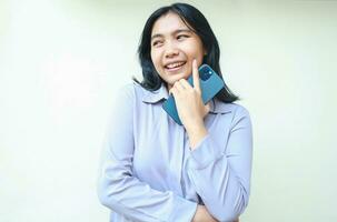 portrait of thoughtful positive asian young business woman holding cell phone thinking plan with dreamy face, daydreaming female wear formal shirt using social media isolated over white background photo