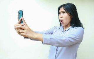 amazed asian young business woman using smartphone shocked with wow expression wearing formal shirt standing over isolated white background photo