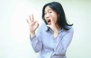 image of satissfied asian young business woman screaming to camera with open mouth giving ok sign with excitement wear formal purple shirt standing over isolated white background photo