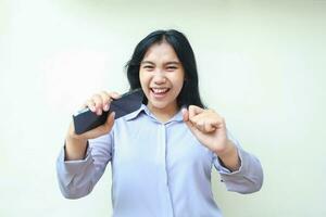 excited asian young business woman holding mobile phone and raising fist pump say yes gesture winning achievement, celebrate victory with dancing, wearing formal shirt standing over white background photo