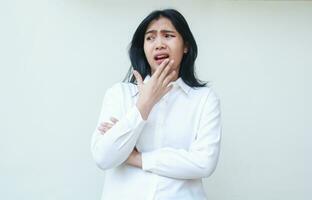 image of shocked asian woman manager wearing white suit shirt looking away stunned unsure with hands on chin arms folded, standing anxious making mistakes, amazed expression photo