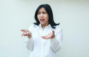 sad asian young woman manager do questioning gesture with shrugs shoulders and keep palms sideways feeling displeased with frowning face, wearing formal white shirt standing ove isolated background photo