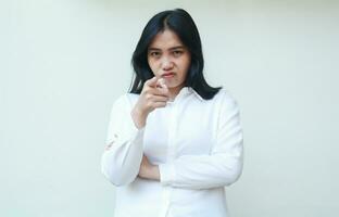 image of displeased asian young business woman pointing and looking at camera with glare, angry and blame you gesture with folded arms, wear white formal shirt standing over isolated background photo