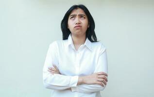 image of desperate asian business woman crossed hand arms folded wearing white suit shirt looking up hoping and wishing expresion, thinking problem and mistake of her job while standing photo