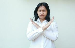 portrait of sad angry asian business woman crossed arms gesture showing rejection, denial, wrong, stop sign wearing white formal shirt standing over isolated background. Human negative symbol concept photo