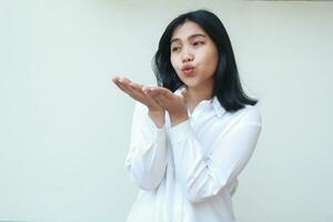 image of pretty calm asian business woman blowing kiss sending love with open palm raising near lips wearing white formal shirt standing over isolated background, candid positive expression, look away photo