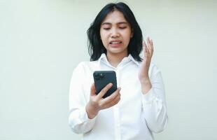 studio shot of disappointed asian young business woman holding smartphone, angry secretary impatient surfing social media and online shopping, raising palms wearing formal white suit, standing photo