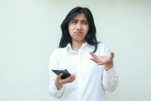 image of sad asian business woman manager holding mobile phone looking aside wondering confused with raising palms wearing white formal suit, have no idea gesture, questioning, standing photo