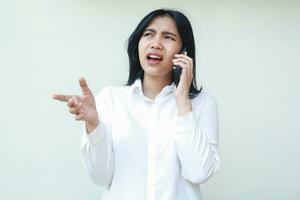 dissatisfied asian young business woman speaking on smartphone having wireless online conversation, wearing white formal suit raising palm asking questioning gesture, disbeliefe expression, standing photo