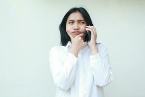 image of thoughtful asian business woman speaking on smartphone having online conversation, thinking strategy plan idea with hands on chin look away, wear formal white shirt, standing photo