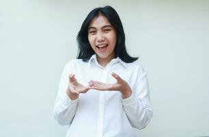 playful succes asian young business woman excited raising hands palms showing imaginary product with happiness face expression wearing white formal suit shirt isolated on white background photo