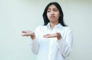 portrait of pondering asian young business woman executive wearing white formal shirt looking away daydream with shrugging shoulders raising open palms, showing and presenting gesture photo