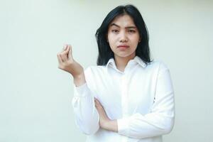 portrait of confused asian young business woman manager looking at camera wondering with raising arm and curled up fingers wearing white formal shirt, standing questioning disbelief gesture photo
