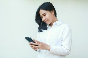 grateful pretty asian business woman satisfied using smartphone apps for online shopping wearing white formal suit shirt, browsing social media, read good news, standing over isolated background photo