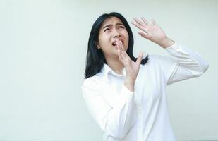 portrait of terrified asian business woman raising palms and looking up with scared face expression wearing white shirt formal suit standing over isolated background photo