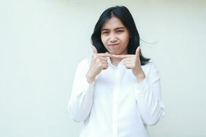 studio shot of gloomy cute asian business woman stick finger together wearing white shirt formal suit looking at camera show demanding expression standing isolated photo