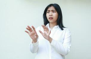 portrait of shocked asian business woman reaching hands towards camera looking away confused and afraid wearing white shirt formal suit standing isolated background photo