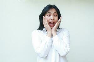 portrait of shocked happy asian business woman surprised looking aside to empty face with reclinings face on hands wearing white shirt formal suit standing isolated background photo