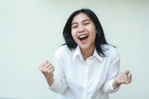 close up of enthusiastic asian woman raising fist show yes gesture wearing wearing white shirt formal suit, ecstatic employee screaming celebrate victory to camera, isolated on white background photo