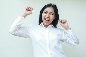 successful asian woman showing yes gesture by raising fist, champions rejoicing win victory wearing white shirt formal suit isolated onw htie background photo