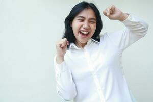 ecstatic enthusiastic asian business woman raising fist showing yes gesture celebrating her success wearing white formal shirt isolated on white background, champion dance photo