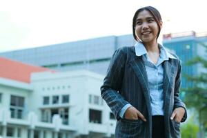 image of successful asian business woman walking in city streets with urban building background looking away confident wearing formal suit, female investment manager standing in outdoors smiling photo