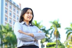 success asian businesswoman wear formal suit cross hand standing over urban building, agent insurance smiling confident looking away show optimistic expression photo